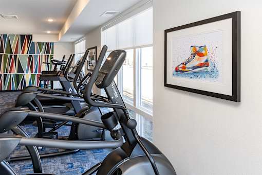 A row of treadmills in a gym with a colorful wall and a framed picture of a shoe on the wall.