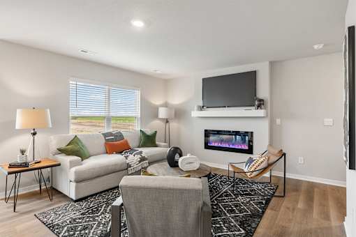 A living room with a grey couch, a black and white rug, a television and a fireplace.