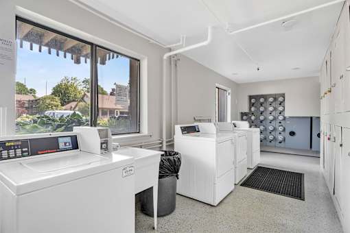 A clean, white-walled laundry room with a washer and dryer, a window, and a view of the outdoors.