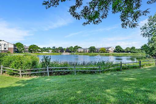 A serene landscape with a lake, greenery, and a fence.