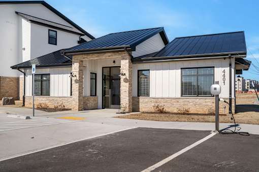 A modern building with a stone pillar entrance and a parking lot in front.