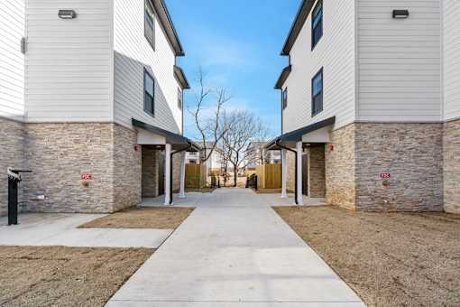 A long concrete walkway separates two buildings with stone pillars.