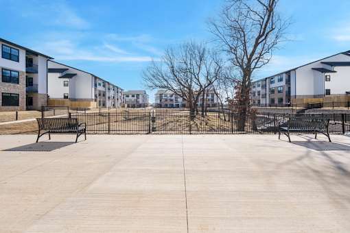 A concrete courtyard with benches and a fence in front of apartment buildings.