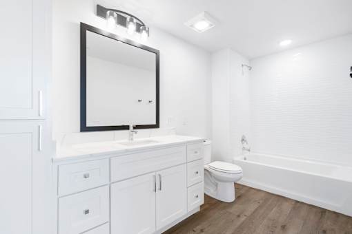 A white bathroom with a mirror, sink, toilet, and bathtub.