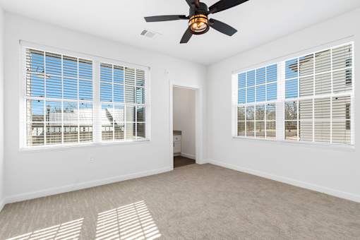 A room with a ceiling fan and two windows with blinds.