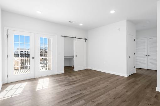A room with white walls and wooden flooring, with a view of a building outside through the windows.
