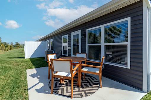A small table and two chairs are on a patio outside a house.