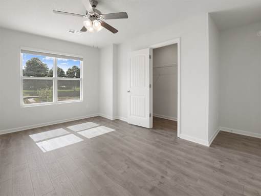 A room with a ceiling fan and a large window overlooking a green area.