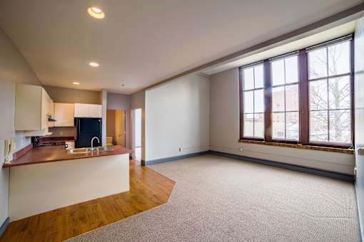 A large, empty room with a kitchen area and a window.