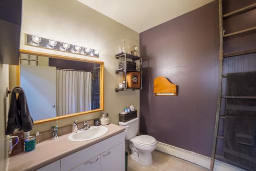 A bathroom with a toilet, sink, mirror, and lights.