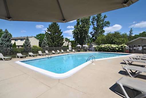 A large outdoor swimming pool surrounded by lounge chairs and trees.