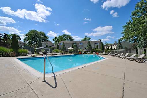 A swimming pool surrounded by chairs and trees.
