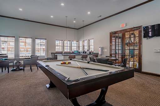 A pool table is in the middle of a room with a door on the right.