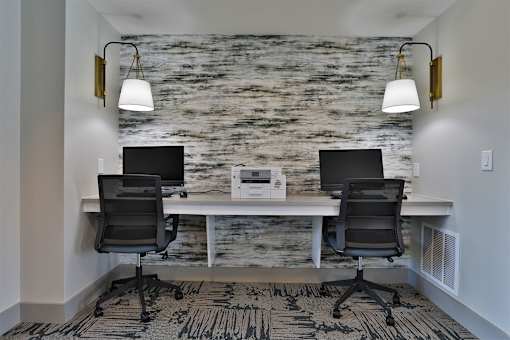Two black chairs are positioned in front of a white desk with a laptop and monitor on it.