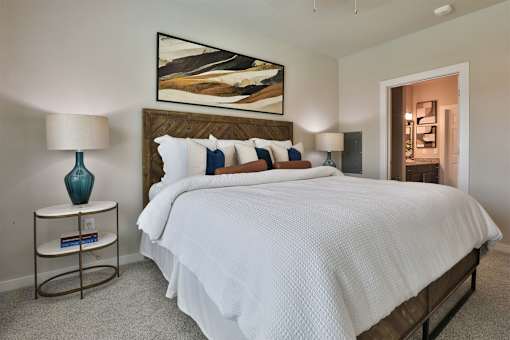 A bedroom with a large bed, a nightstand with a lamp, and a painting on the wall.