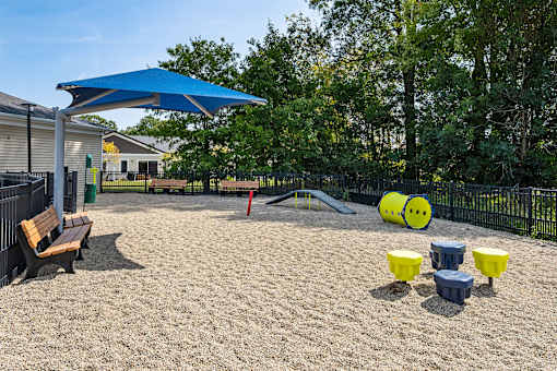 A playground with a blue umbrella, yellow and blue containers, and a slide.