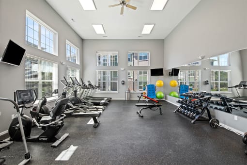 a gym with cardio machines and windows and a ceiling fan