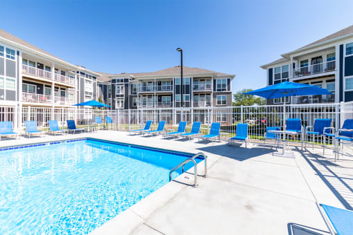 a swimming pool with blue chairs and umbrellas in front of a building