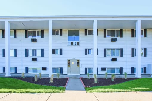 a white apartment building with a sidewalk and grass