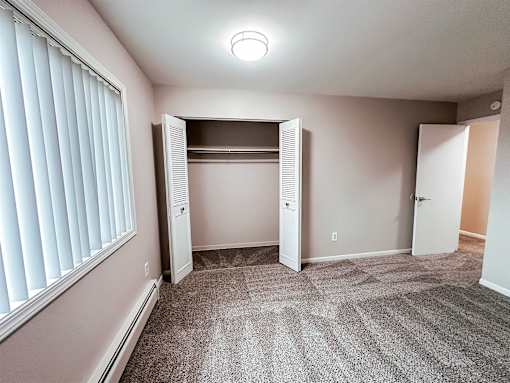 A room with a carpeted floor and a window with blinds.
