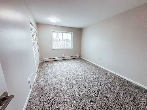 A room with a carpeted floor and a window with blinds.