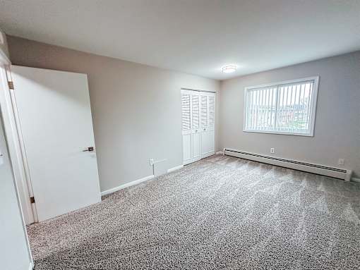 A room with a carpeted floor and a window with blinds.