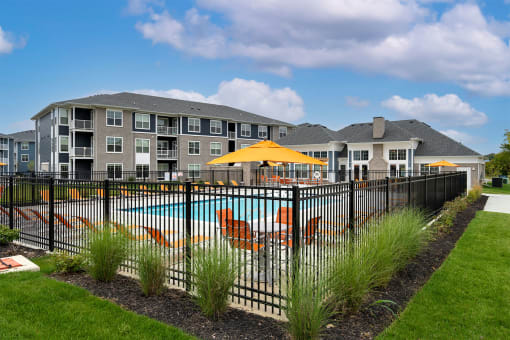 a pool with chairs and an umbrella in front of an apartment building
