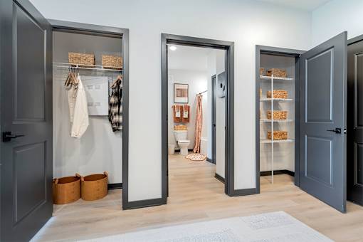 A hallway with a grey floor and a white rug, with three open doors on the left and right.