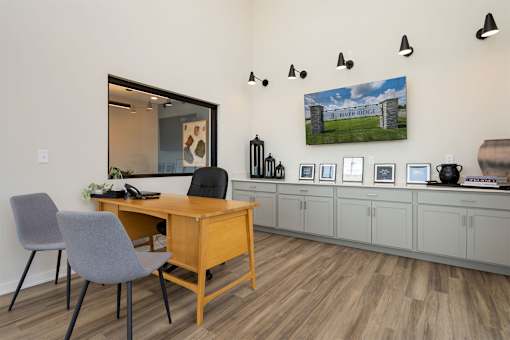 A room with a desk and chairs with a picture of a river ridge on the wall.