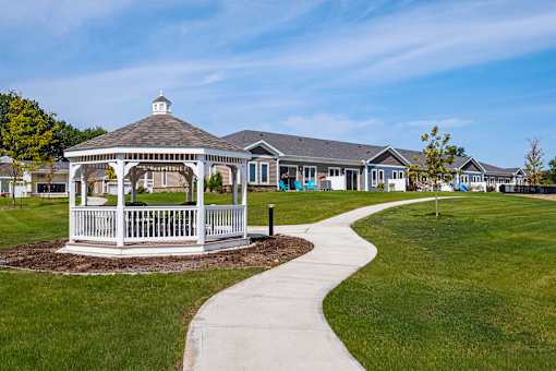 A gazebo is situated in the middle of a grassy area with a walkway leading to a building.
