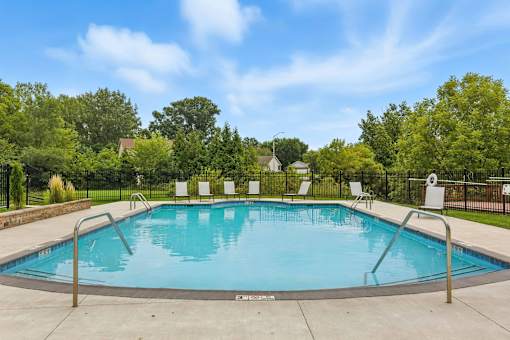 A swimming pool surrounded by trees and chairs.