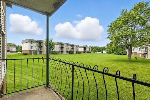 A view from a balcony overlooking a grassy area with apartment buildings in the distance.