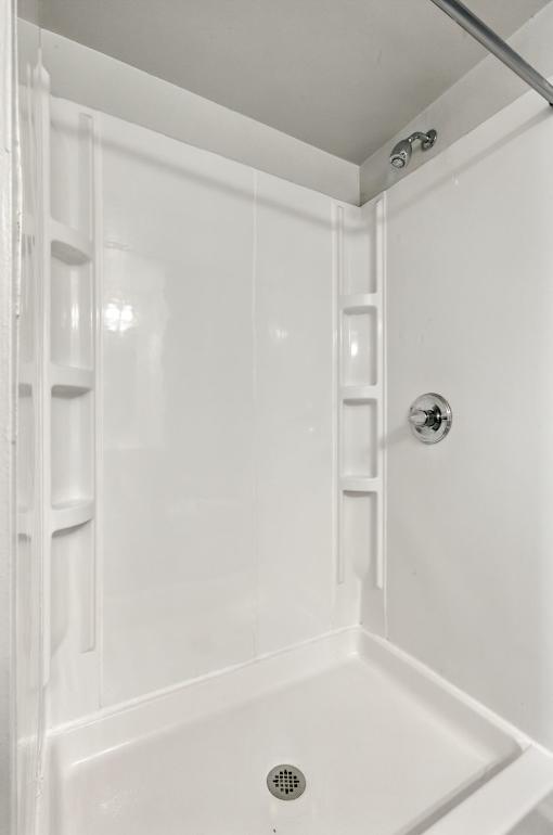 A white bathroom with a shower stall and a drain in the tub.