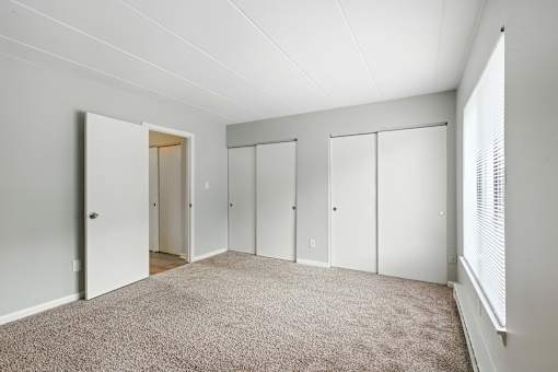 A room with white walls and a carpeted floor with four closets.