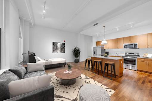 A modern living room with a grey couch, a coffee table, and a kitchen area in the background.