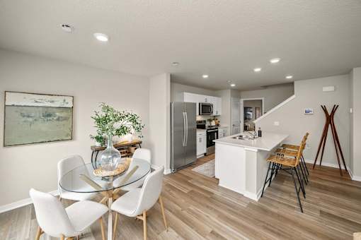 A dining table with white chairs and a glass top is in a room with a wooden floor.