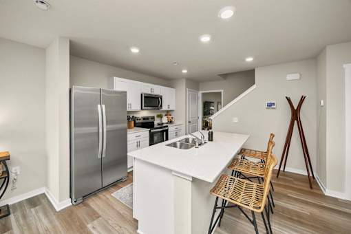 A kitchen with a refrigerator, microwave, and a counter with a chair.