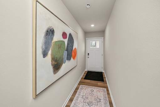 A hallway with a painting on the wall and a rug on the floor.