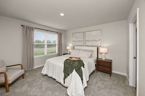 A bedroom with a bed, nightstand, chair, and window.