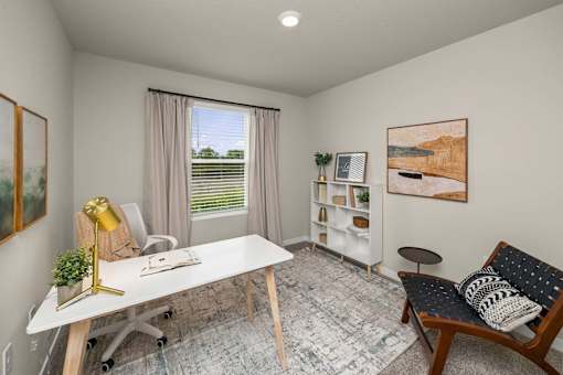 A room with a white desk, a chair, a couch, and a painting on the wall.