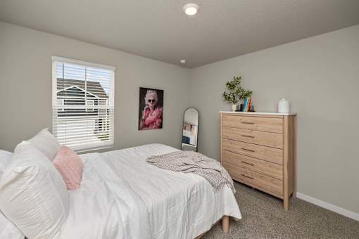 A bedroom with a bed, dresser, and a window with blinds.