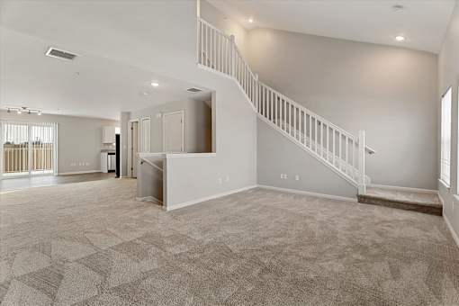 A spacious living room with a staircase and a kitchen area in the background.