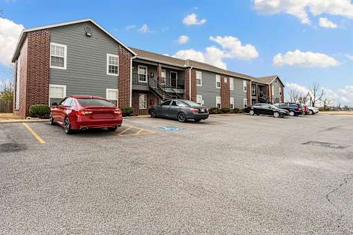 A red car is parked in a parking lot in front of a building.