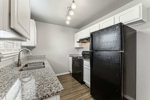 A black refrigerator stands in a kitchen with white cabinets and a granite countertop.