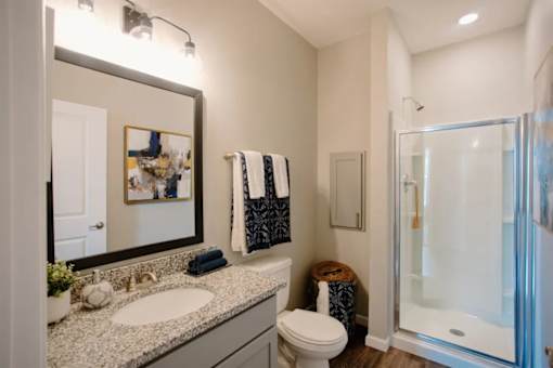 A bathroom with a toilet, sink, mirror, and a glass shower door.