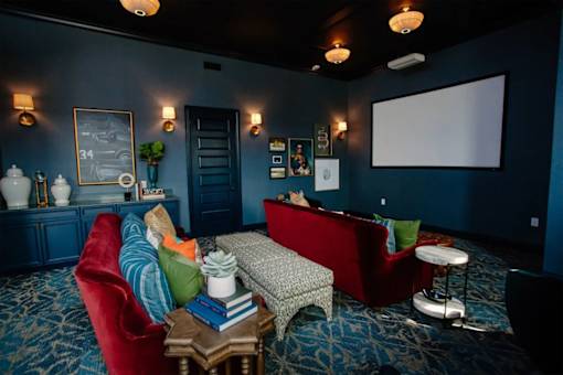 A room with a red chair and a grey sofa with a person sitting on the sofa.