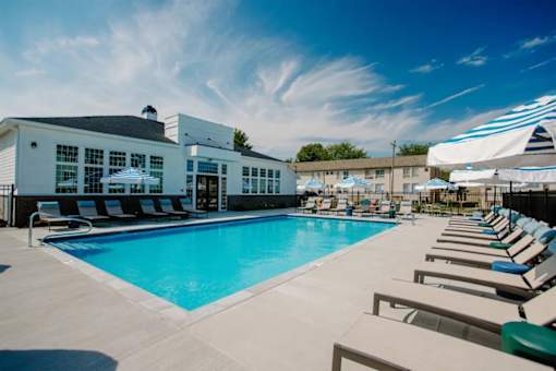 A large swimming pool area with sun loungers and a building in the background.