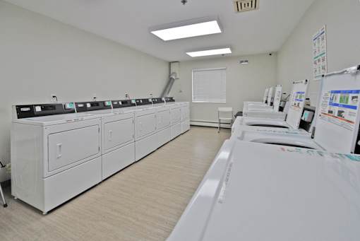 A clean, white-walled room with a series of white appliances on the left and a white washing machine on the right.