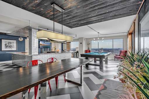 A pool table is in the middle of a room with a wooden table and red chairs.