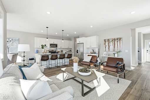 A modern living room with a white couch, a coffee table, and a kitchen area in the background.